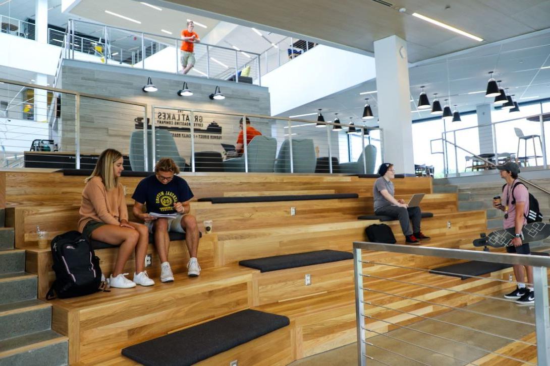 Multiple groups of students study and chat while seated on wooden benches inside Kettering's Learning Commons